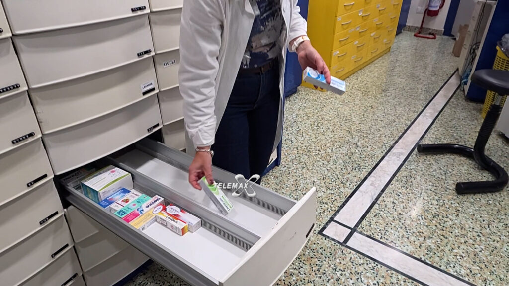Una farmacista in camice preleva una confezione di farmaci da un cassetto della cassettiera di una farmacia