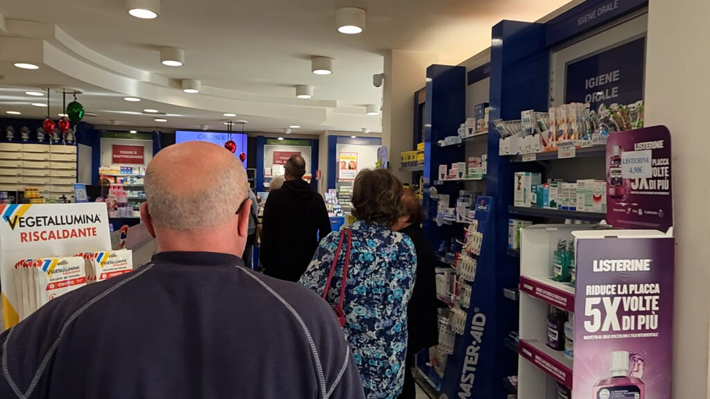 Clienti in attesa del proprio turno tra gli scaffali di una farmacia